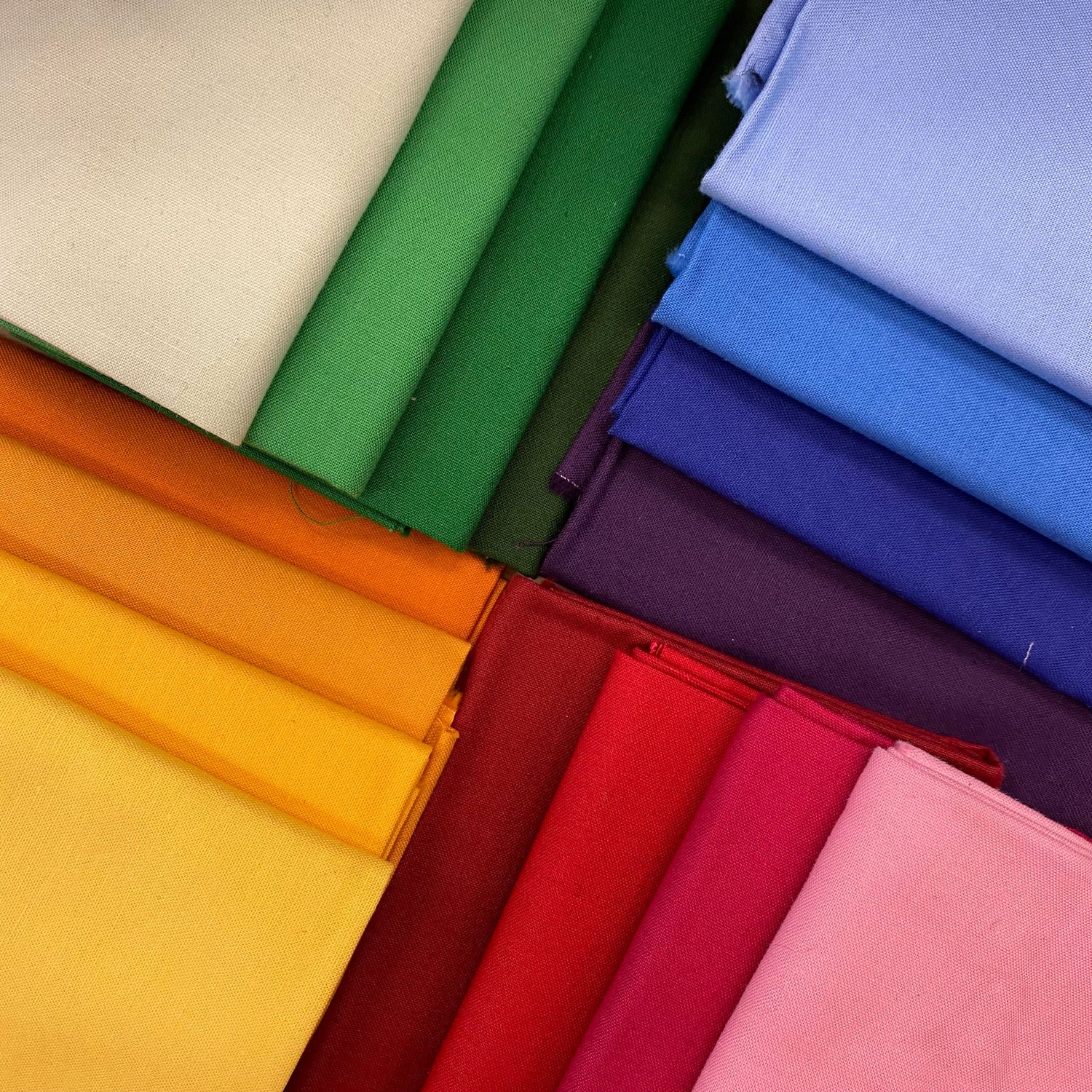 Fabric Collection Banner image includes 16 colors of solid fabric, laid out in a 4 color groups with darkest on bottom and lightest on top and arranged around a central point. Stitcher's Joy