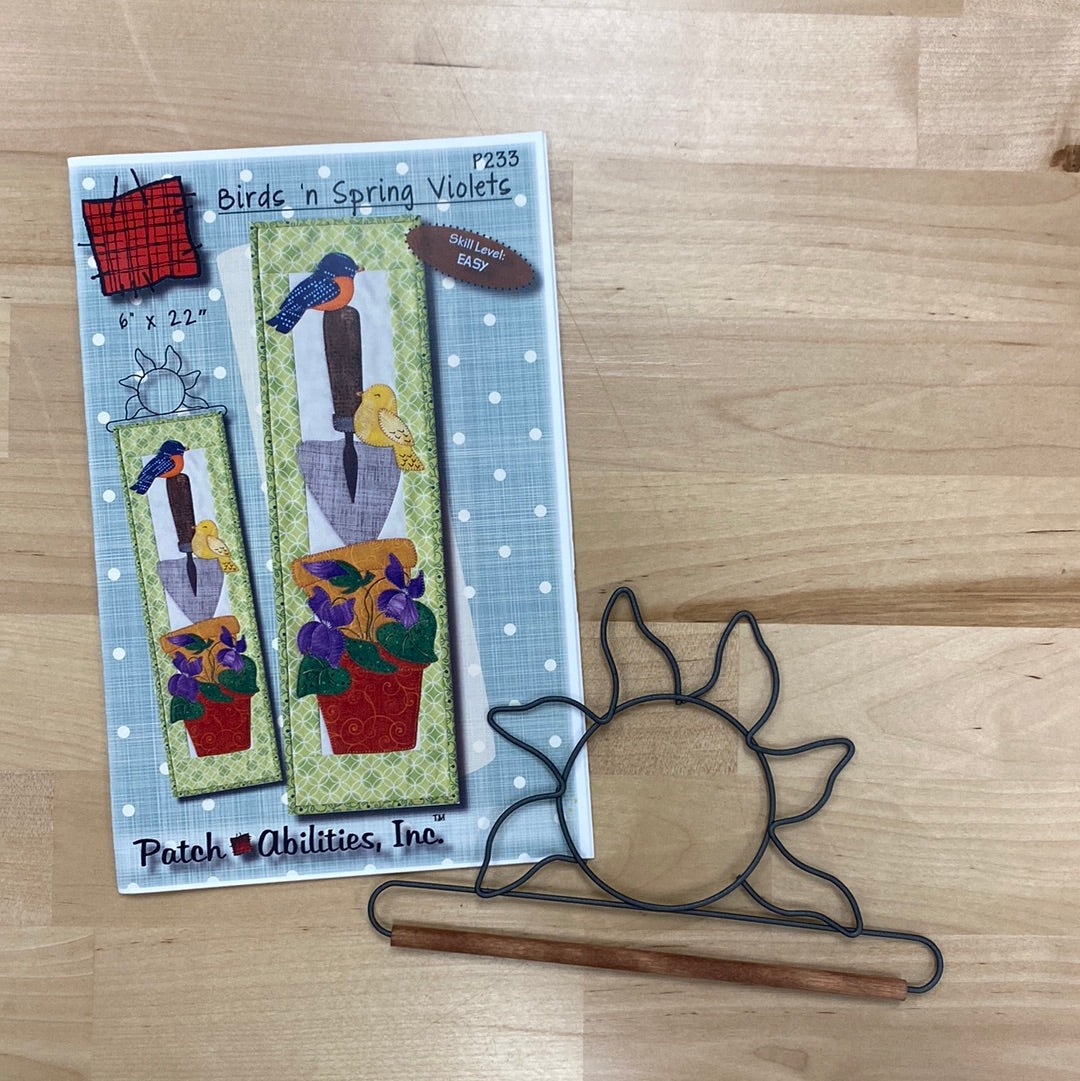 Decorate your home for Spring with the mini quilt applique pattern, Birds ‘n Spring Violets (P233) by PatchAbilities! A garden lovers scene with terra cotta pots, a gardening spade, violets, and birds. Photo shows the pattern front with the included sun hanger.