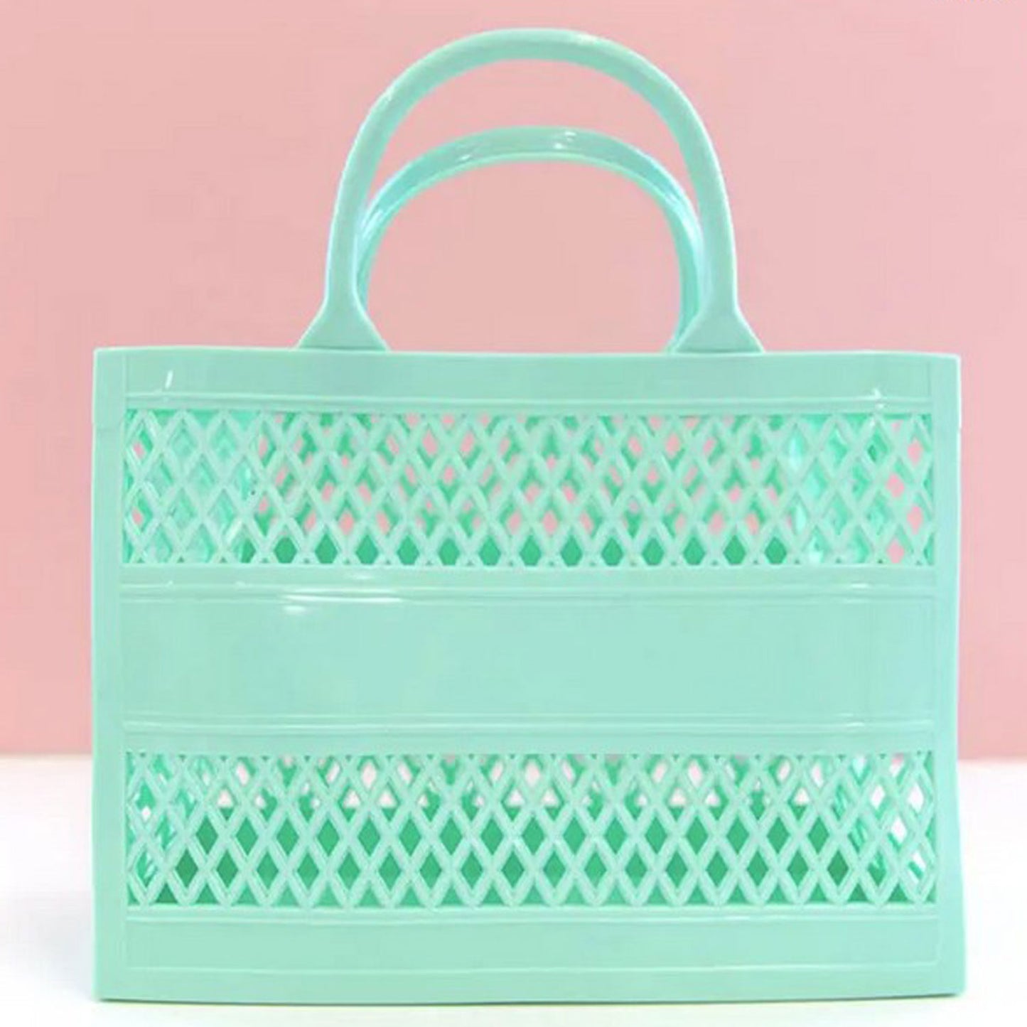 Made of durable PVC, this Mint Green tote is the jelly material from the 80's. Photo shows the tote against a pink and white background.