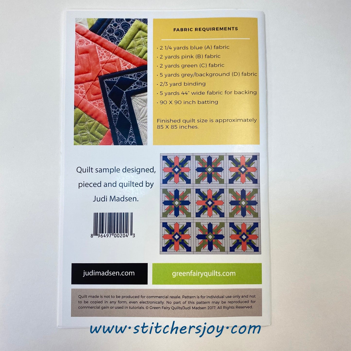 The Free Spirit Pattern back cover by Judi Madsen of Green Fairy Quilts includes the fabric requirements to complete an 85" x 85" quilt. An additional photo showcases the geometric shapes surrounded by fill quilting, that was used on the cover quilt. The thread blends with the white background while highlighting the quilting on the colored pieces. A second photo shows the 9x9 layout with the two different colorways for the alternating blocks.