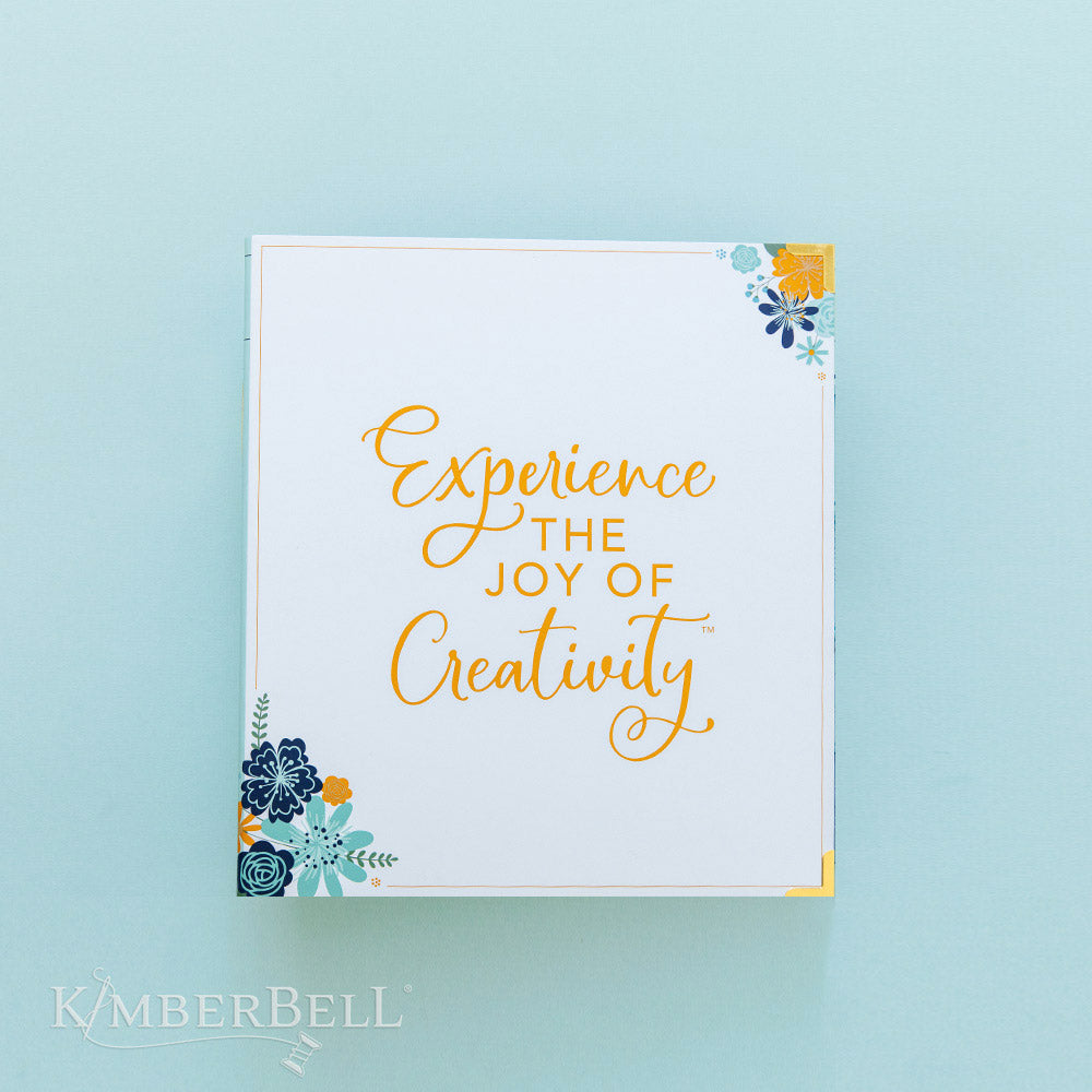 This binder by Kimberbell is the perfect place to keep your Kimberbell instructions or loose CD's and USB drives. This picture shows the front of the binder with "Experience the Joy of Creativity" and blue and orange flower grouping in the upper right and lower left corners.