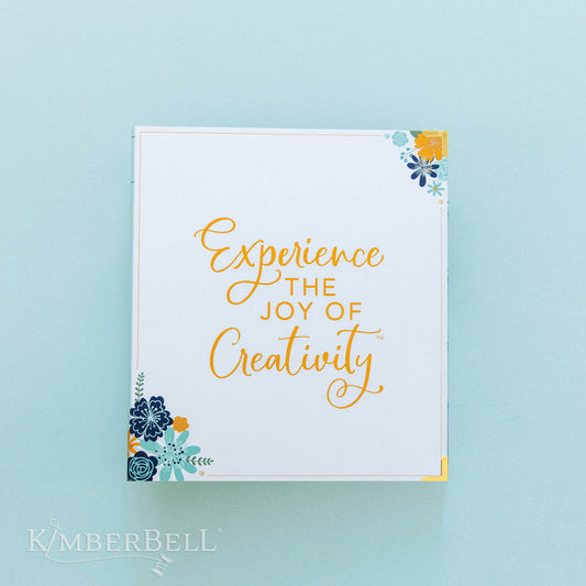 This binder by Kimberbell is the perfect place to keep your Kimberbell instructions or loose CD's and USB drives. This picture shows the front of the binder with "Experience the Joy of Creativity" and blue and orange flower grouping in the upper right and lower left corners.