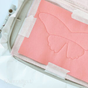 Paper Tape (KDTL100) by Kimberbell is perfect for in-the-hoop, machine embroidery projects. The use of the semi-transparent tape holding fabric to stabilizer in the hoop is shown.