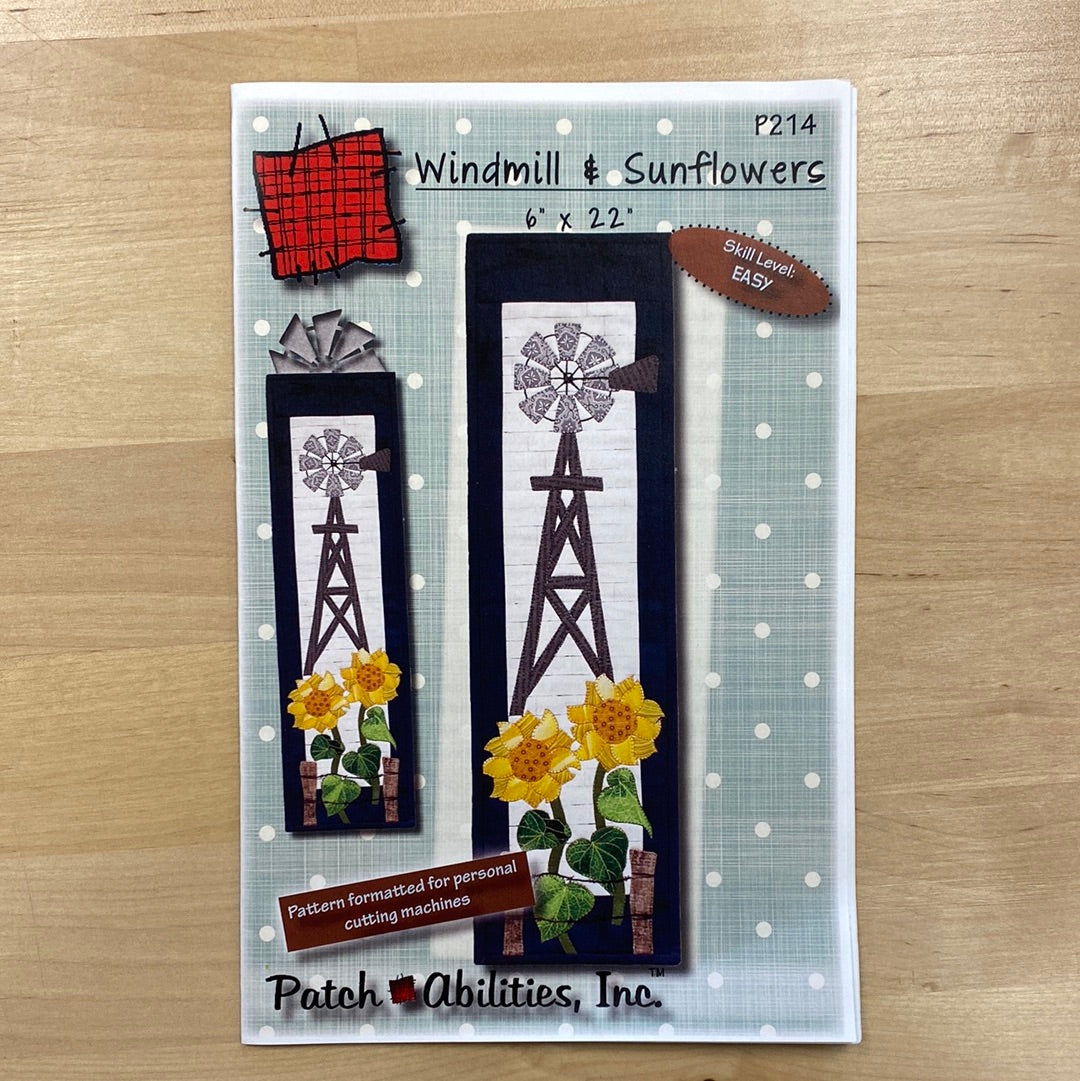 This Windmill & Sunflowers (P214) mini quilt pattern by PatchAbilities features a rustic windmill with graceful sunflowers behind a barbed wire fence. Photo shows the front cover of the pattern.