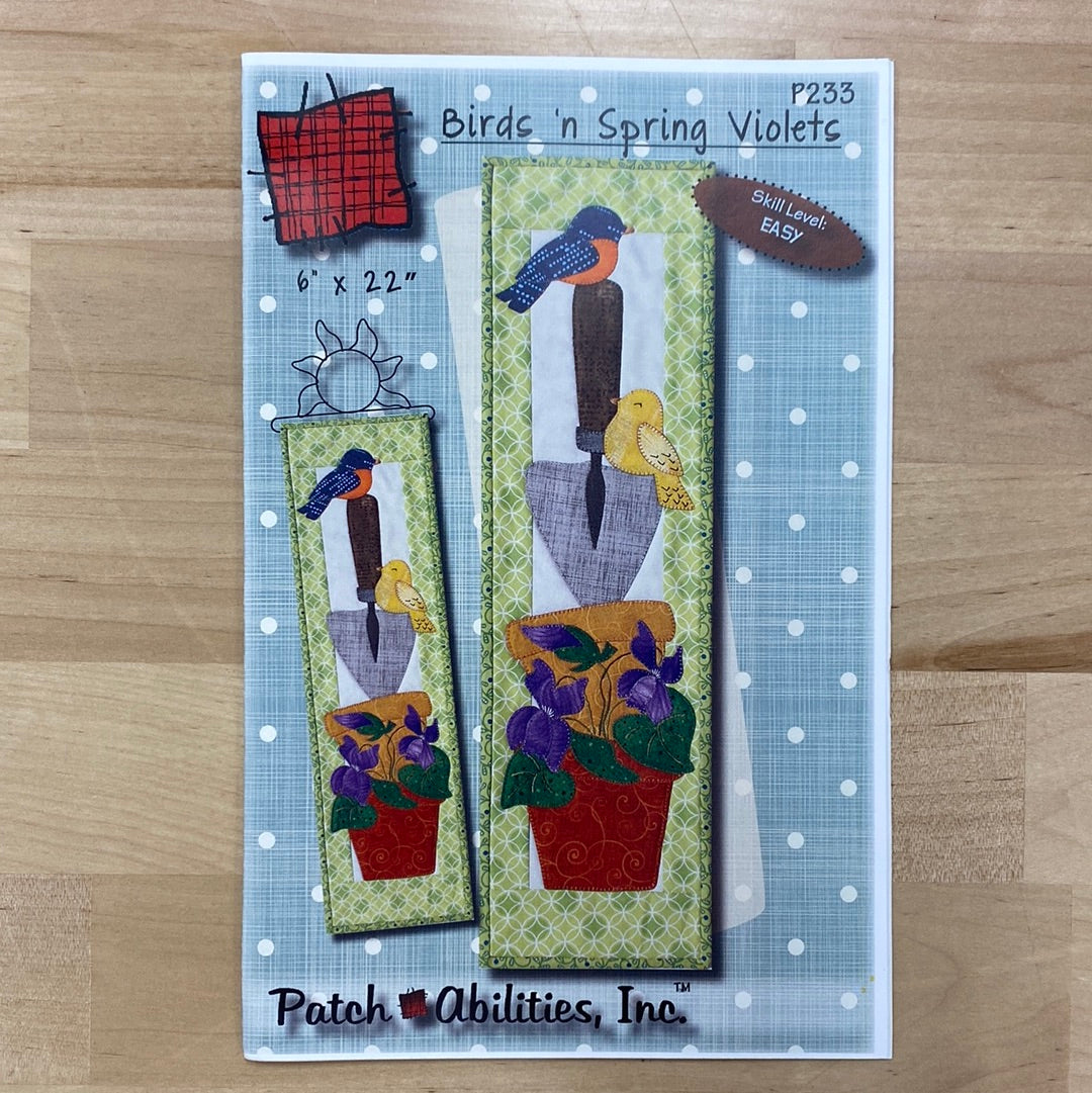 Decorate your home for Spring with the mini quilt applique pattern, Birds ‘n Spring Violets (P233) by PatchAbilities! A garden lovers scene with terra cotta pots, a gardening spade, violets, and birds. Photo shows the pattern front.