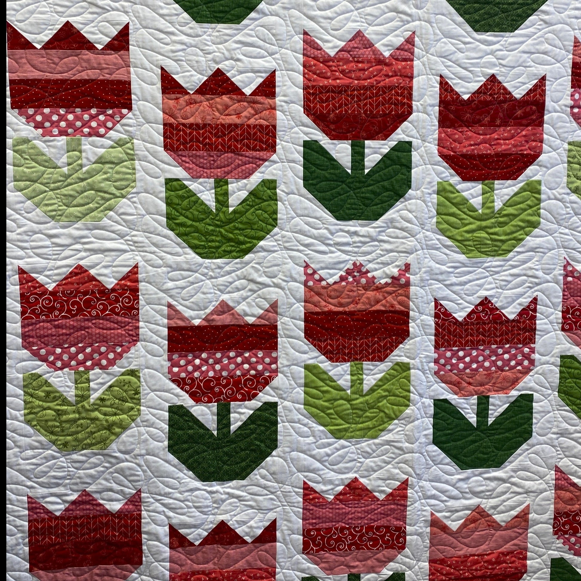 This quilt features rows of tulips with red strips used for the flower and various greens used for the stems. They are created in columns with stair-stepped rows on a white background with a light green binding.