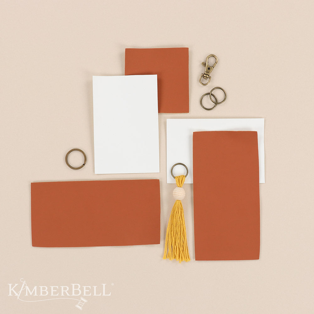All the darling details for your What’s the Buzz key-chain project in one kit (KDKB1283)! Create your key-chain and lip balm holder with brass key-chain hardware, jump rings, a mustard tassel with bead, and Embroidery Leather in camel and white colors. Photo shows the contents of the package.