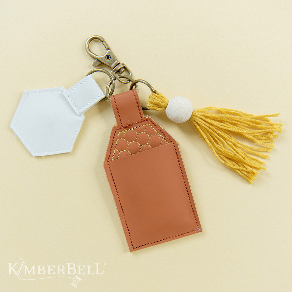 All the darling details for your What’s the Buzz key-chain project in one kit (KDKB1283)! Create your key-chain and lip balm holder with brass key-chain hardware, jump rings, a mustard tassel with bead, and Embroidery Leather in camel and white colors. Photo shows the assembled product.