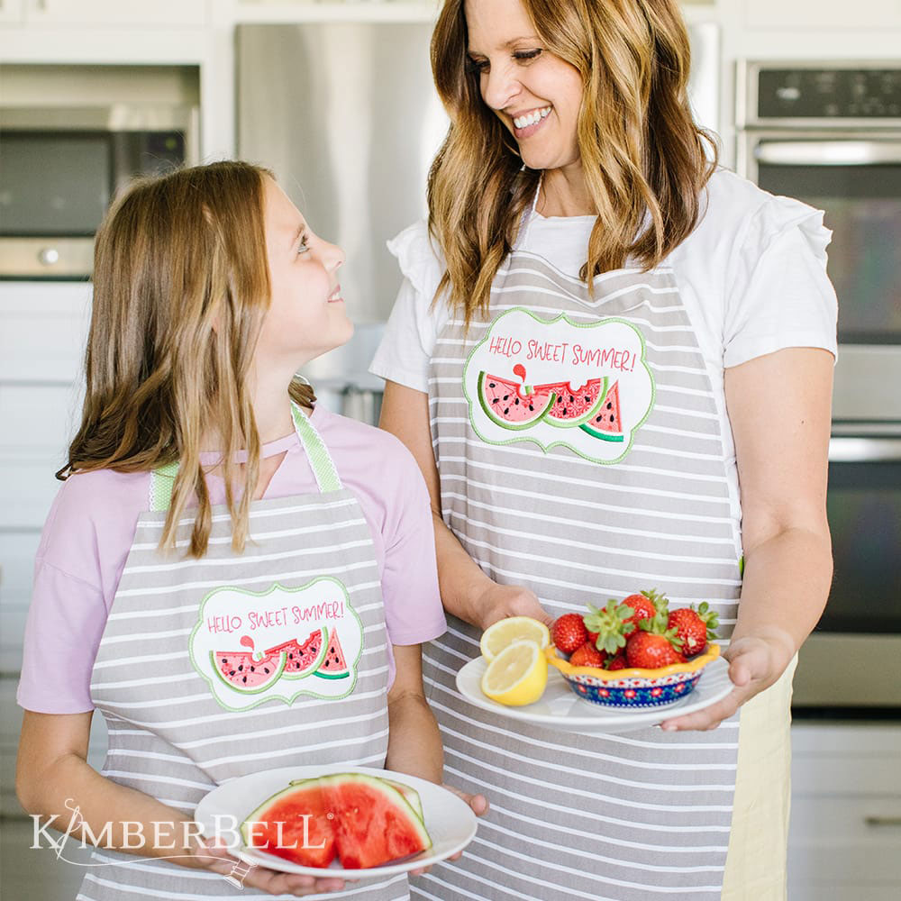 Kimberbell Over the Edge Applique for Spring and Summer (KD588) features 3D applique, plaques, and fun pockets. This photo shows the a plaque with watermelons and the words Hello Sweet Summer! appliqued to the front of two aprons.