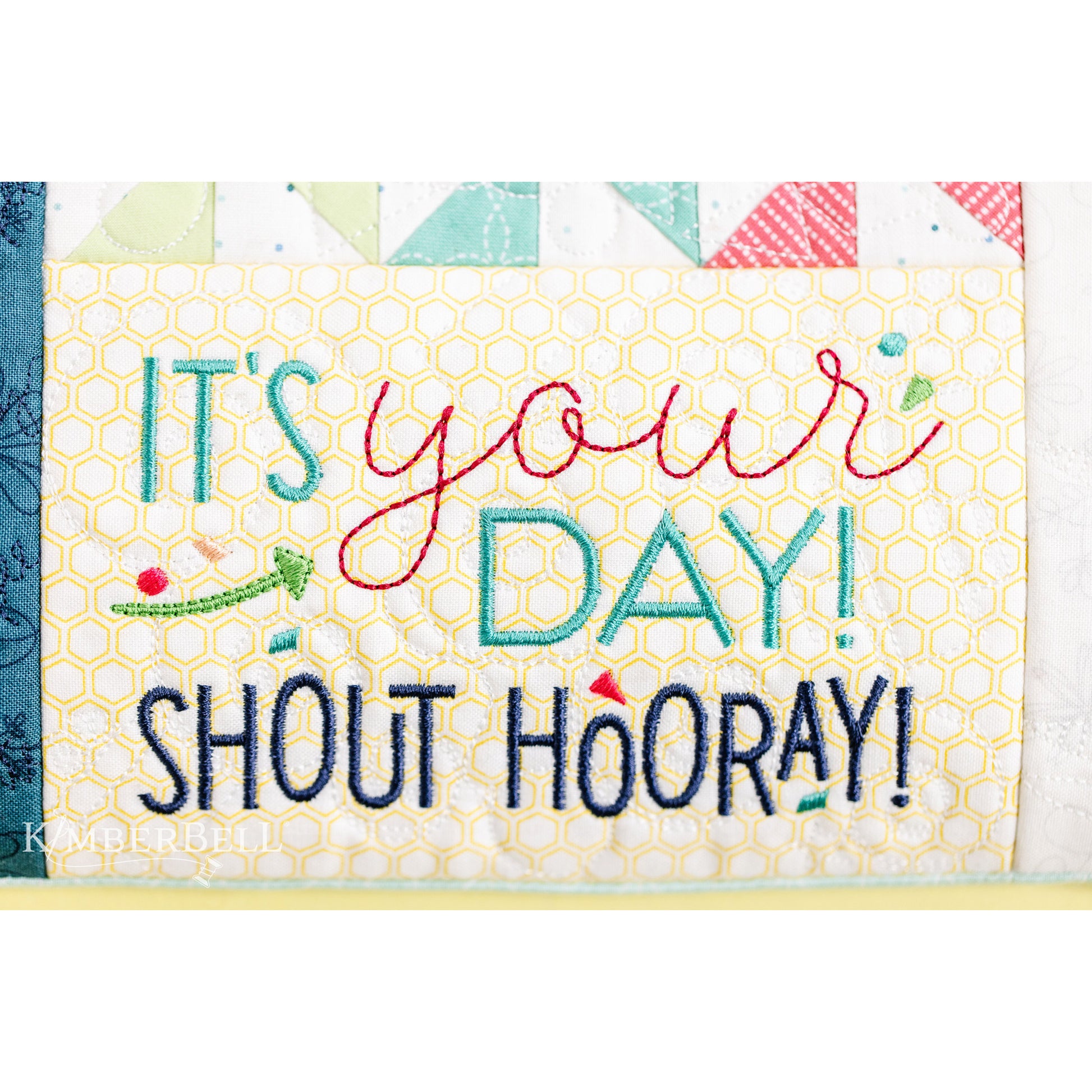Kimberbell’s Shout Hooray! Bench Pillow Pattern (KD5120) celebrates the people you love with confetti, cake, and more! Stitch names, dates, and greetings with the included alphabet and sentiments, then feature your message in the letterboard panel. Image shows the "Shout Hooray" finished block.