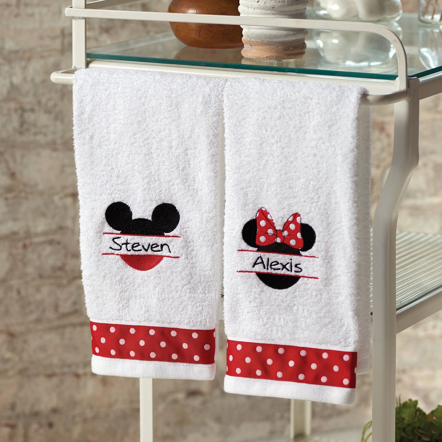 White bath towels embroidered with Mickie and Minnie Mouse designs with red polka dot accents.