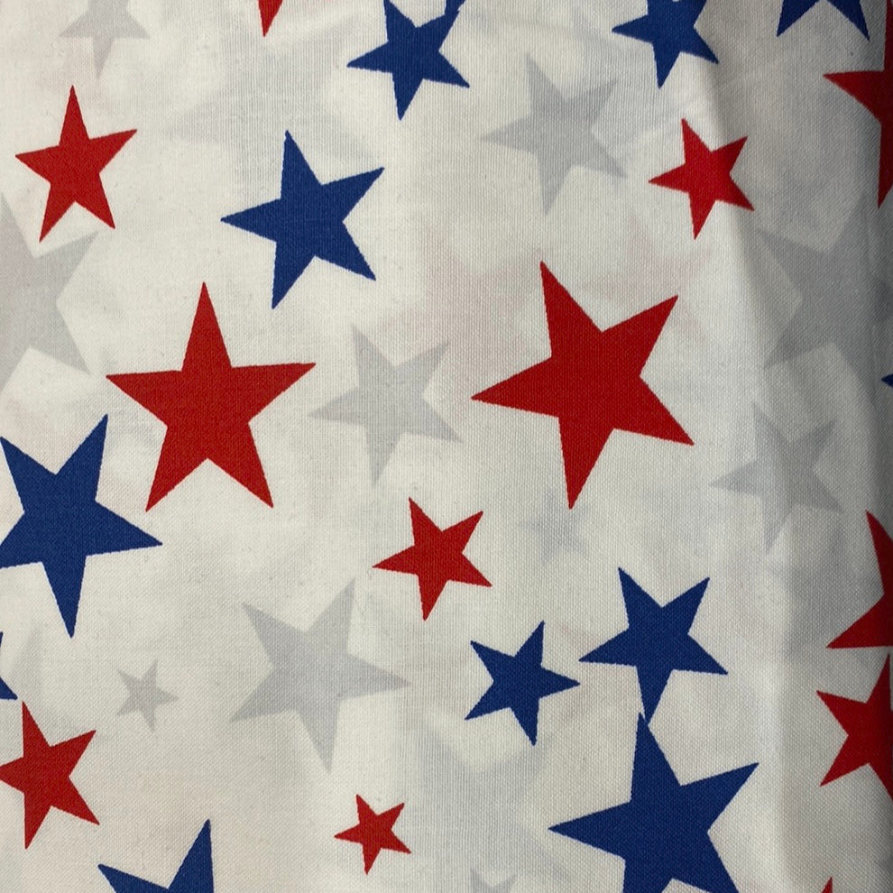 This wide back fabric is 108" wide, and is cut to a 3 yard length, making it 108" x 108". It features a white background with different sized red and blue stars in a scattered pattern. Photo shows a sample of the fabric.