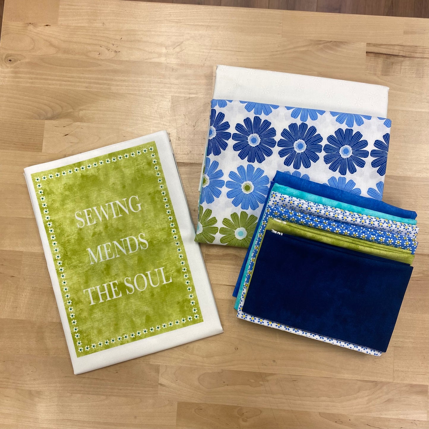 Quilters Chalk Quilt Kit fabric samples, including blue fabrics, ombre daisy border print, white on white background, and Quilters Chalk panel in the blue/green colorway.