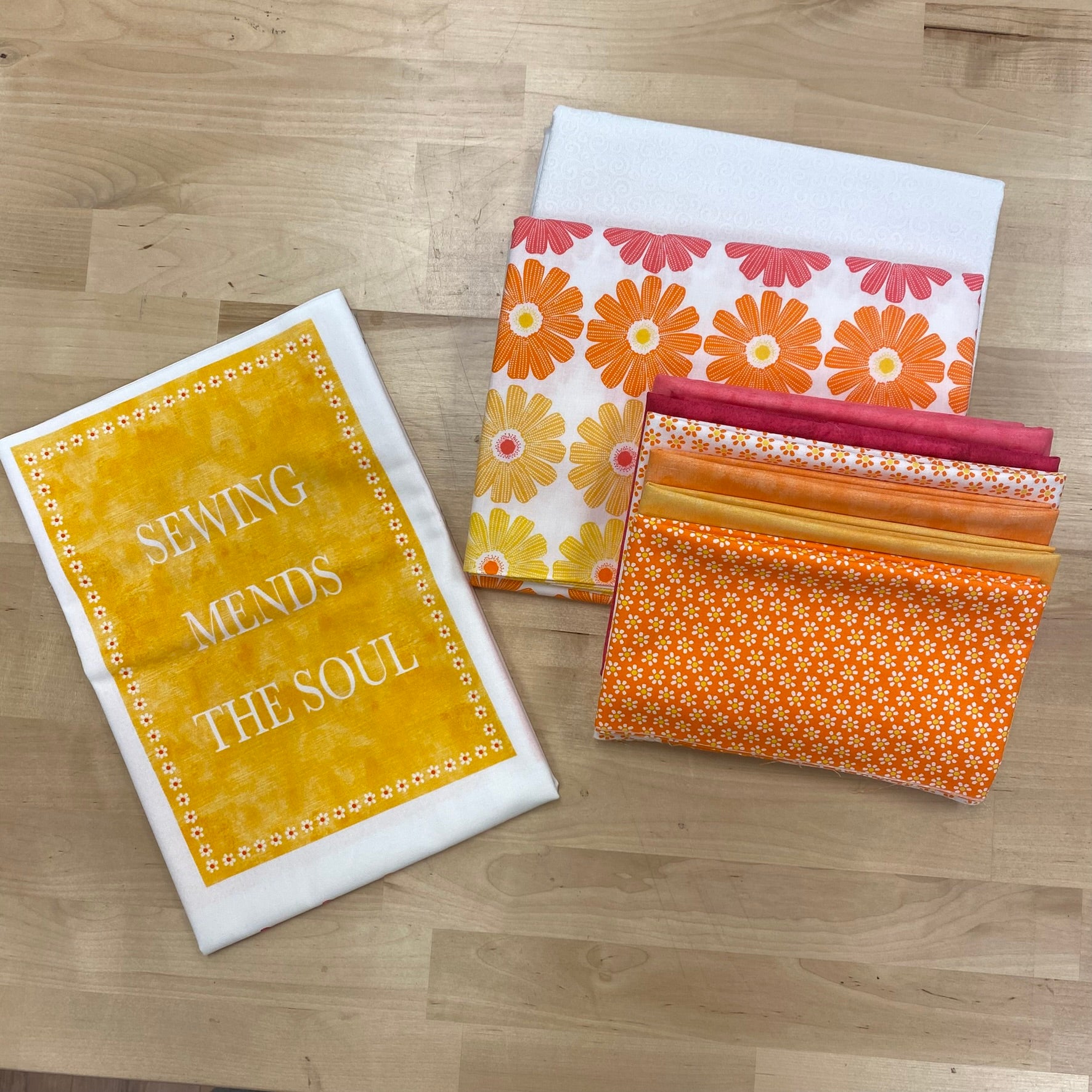 Quilters Chalk Quilt Kit fabric samples, including pink, orange, and yellow fabrics, ombre daisy border print, white on white background, and Quilters Chalk panel in the pink/orange/yellow colorway.