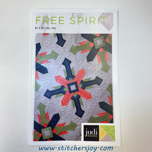 The Free Spirit Pattern front cover by Judi Madsen of Green Fairy Quilts features large blocks with contrasting colors of navy, coral, and olive on a white background. The fabrics are arranged in geomatric shapes layered on top of each other, to create a compass effect with plenty of room to showcase the quilting. Although the quilt uses the same fabrics and same block design, the color placement is shifted to create alternating blocks in two colorways. The cover states the quilt finishes at 85" x 85".