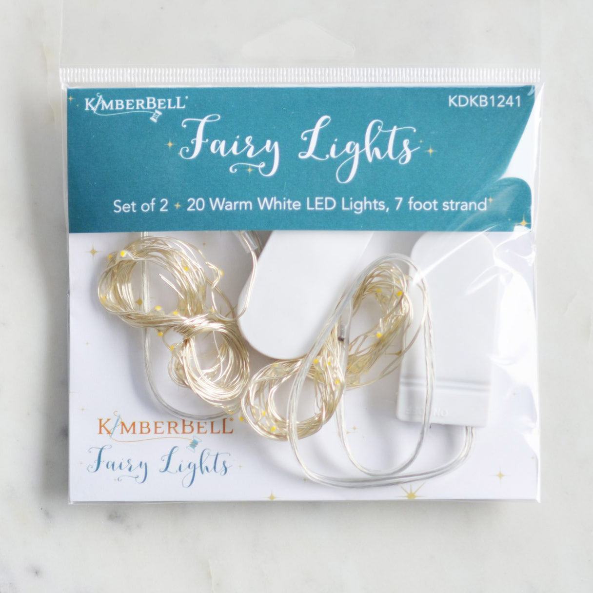 Kimberbell Fairy Lights add a soft glow to projects. Each package contains 2 seven foot strands with 20 warm white LED lights on each strand. Each strand includes a battery pack with on/off switch.