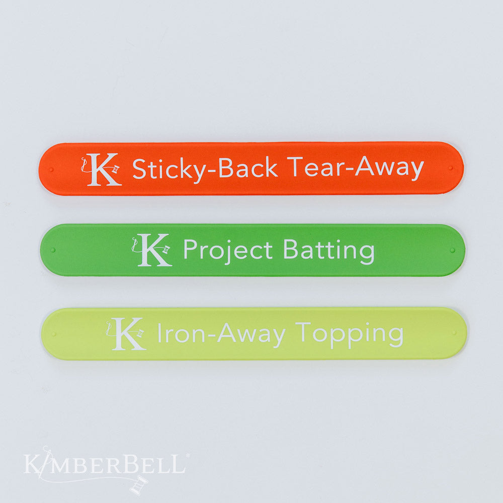 Stabilizer Slap Bands Add-On Set of 3 bands by Kimberbell (KDST142) is an add-on to those who purchased the original set of 13 stabilizers. The image shows the indivudal included bands: Sticky-Back Tear-Away, Project Batting , and Iron-Away Topping