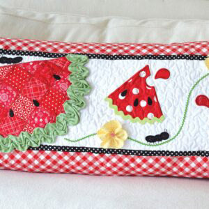 Celebrate summer with the Slice of Summer Watermelon Bench Pillow pattern for machine embroidery by Kimberbell! The scrappy slice of watermelon wedge and slices are adorned with rind “ruching” and ric rac trim with dimensional flowers, while the little applique ants join in the summertime fun.