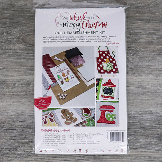 We’ve gathered all the trimmings to complete your We Whisk You a Merry Christmas Quilt in the We Whisk You a Merry Christmas Embellishment Kit (KDKB166). Our delightful embellishment kit is a joy to unwrap, with clear vinyl and applique glitter, designer holiday buttons, marshmallow poms, chalk fabric, and more! Photo shows the back of the package.