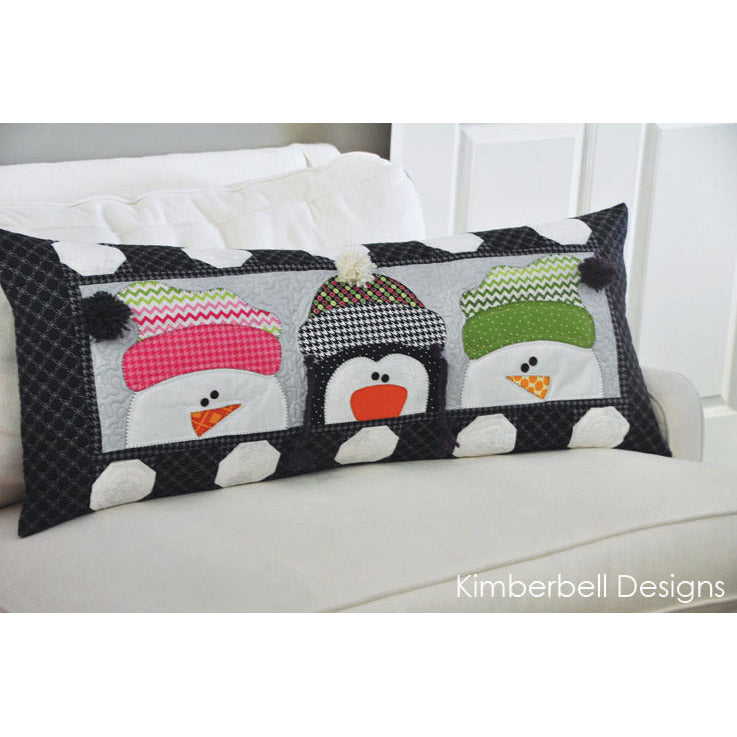 Delightful snowmen and a penguin with their fluffy stocking caps welcome the snow with the Whimsy Winter Bench Pillow Sewing Version (KD164) by Kimberbell. Photo shows the detail of the bench pillow, including 2 snowmen and a penguin with stocking hats with fluffy balls surrounded by a border of pieced snow balls.